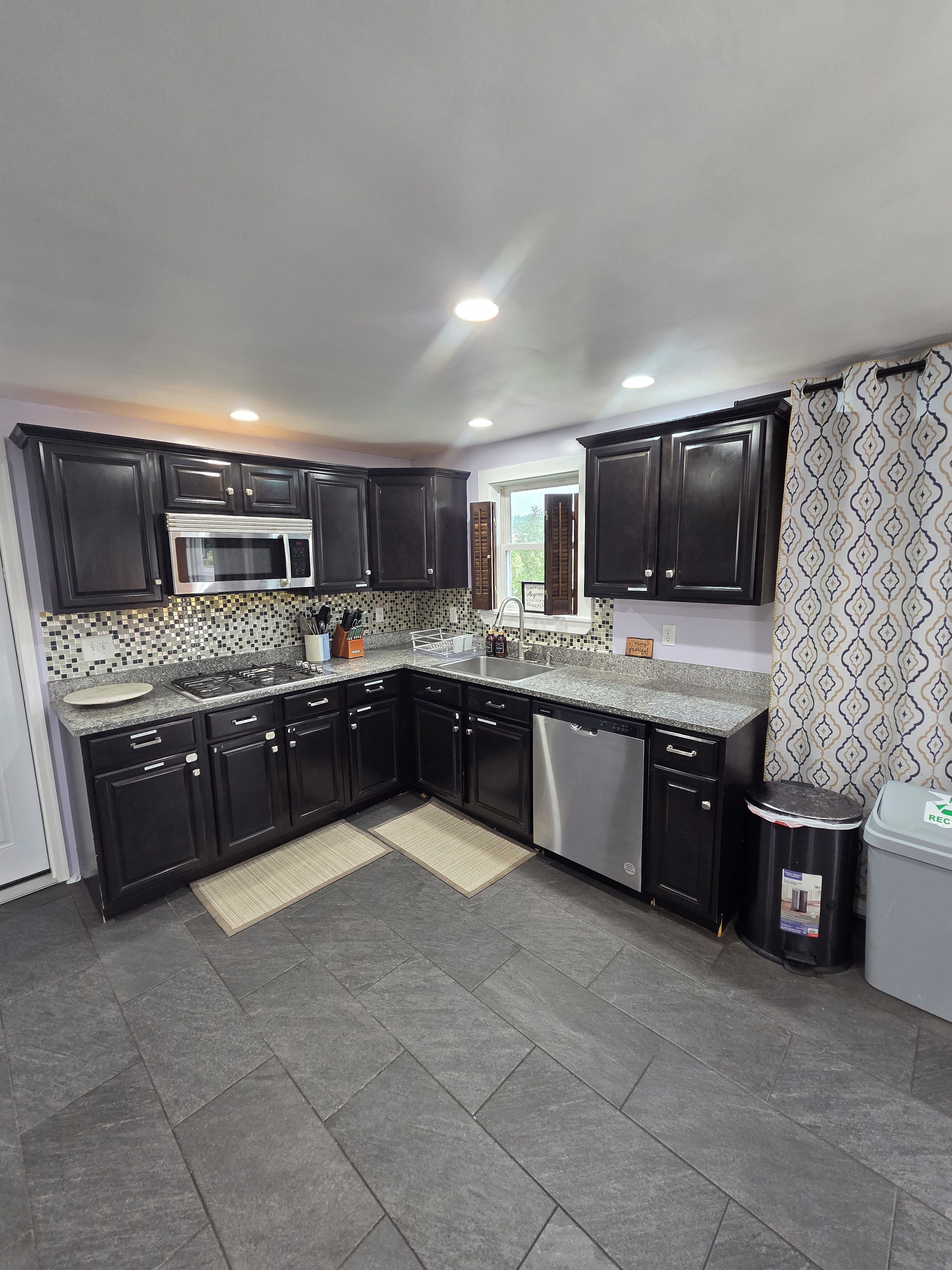 A modern kitchen with dark cabinets, a stainless steel microwave, and a dishwasher.