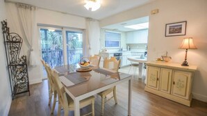 A dining area with a glass table, wooden chairs, a buffet table with food, a kitchen in the background, and a balcony with curtains. - Large & Comfy Beach Apartment with Screened Patio (West Palm Beach)
