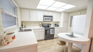 A compact kitchen with white cabinets, a microwave, an oven, a sink, and a dining table with chairs. - Large & Comfy Beach Apartment with Screened Patio (West Palm Beach)