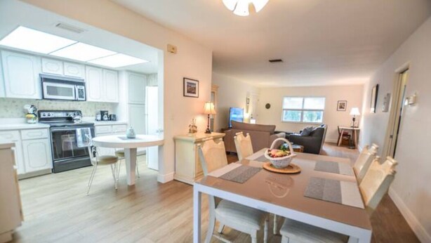 A modern kitchen with white cabinets, a microwave, and a stove. There is a dining area with a table and chairs, and a living room with a sofa and a TV. - Large & Comfy Beach Apartment with Screened Patio (West Palm Beach)