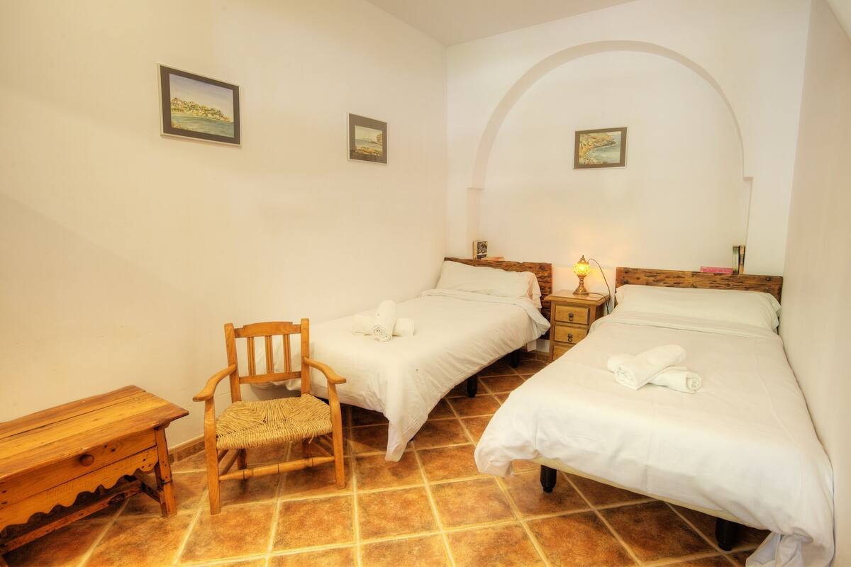 Ein Schlafzimmer mit zwei Betten, einem Holzstuhl, einem kleinen Tisch und einem Nachttisch mit Lampe.