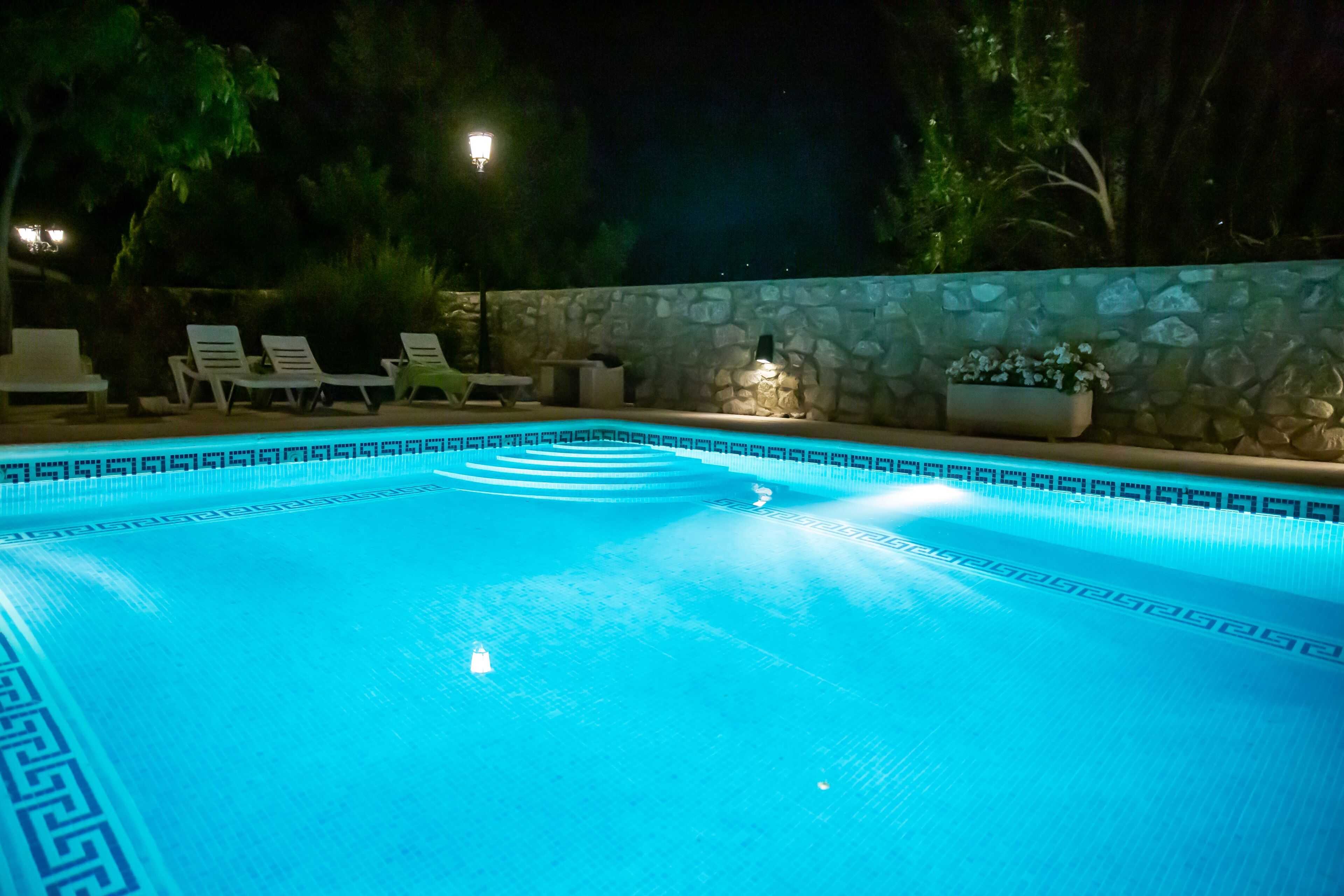 A swimming pool with a stone wall and lounge chairs.