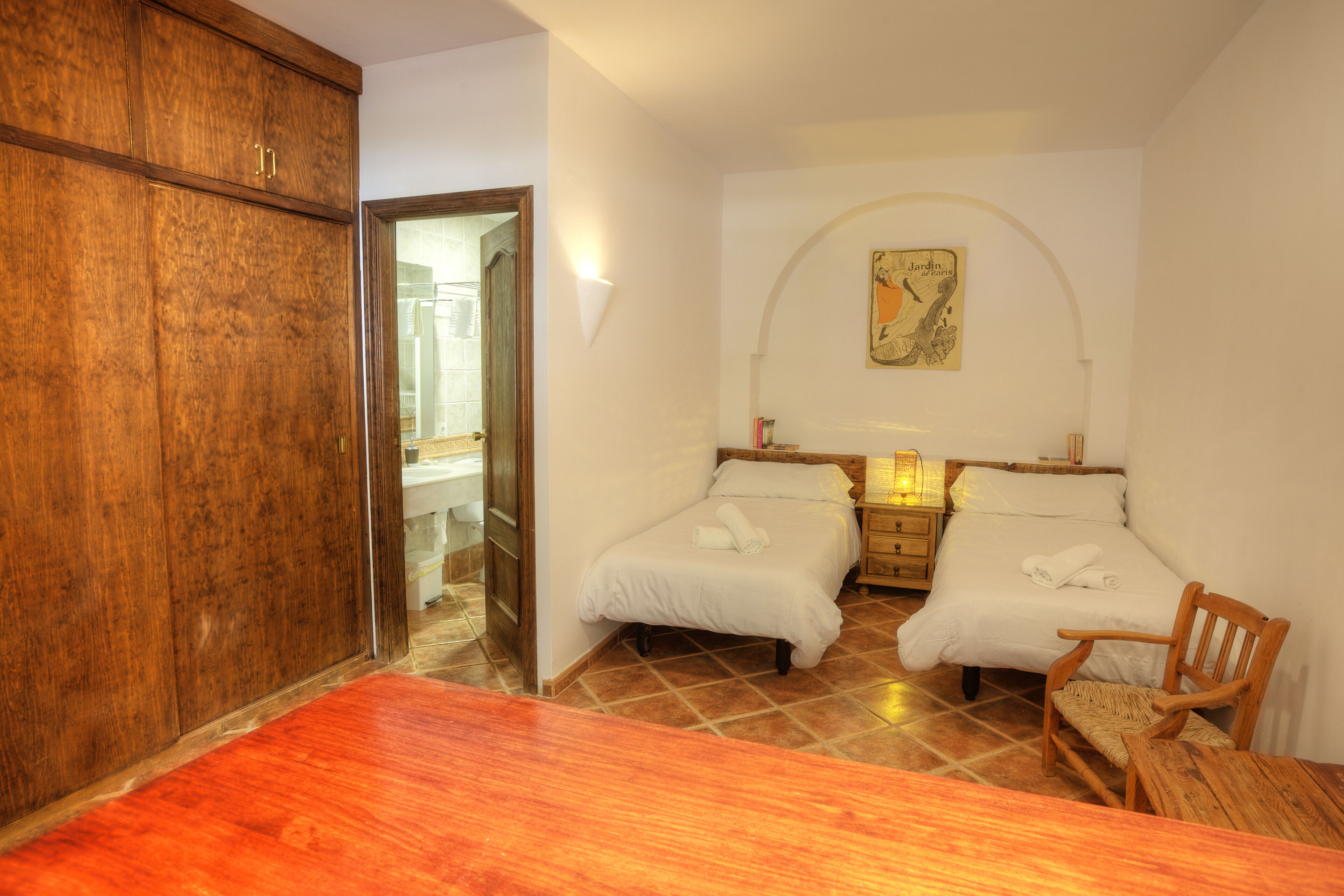 A bedroom with two beds, a wooden wardrobe, a wooden chair, and a wooden table.