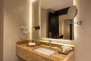 A modern bathroom with a marble sink, a handheld mirror, and a hairdryer mounted on the wall.