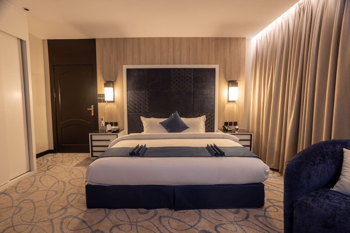 Ein Hotelzimmer mit einem großen Bett, zwei Nachttischen, einem Kopfteil und einem Vorhang auf der rechten Seite.