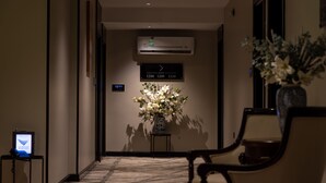 Pasillo de hotel con mostrador de recepción, pantalla digital, arreglo floral y señal con números de habitaciones.