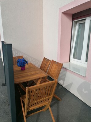 Un juego de mesa de madera y sillas frente a una pared con textura, junto a una ventana y un pequeño balcón.