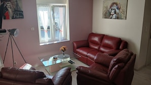 A living room with a red leather sofa, a glass coffee table, and a painting on the wall. - Comfortable rarounette gite in the heart of the Vosges mountains (celles sur plaine)