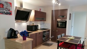 A modern kitchen with wooden cabinets, a built-in oven, a microwave, and a coffee maker. There is a dining table with red cushions and a vase of flowers. - Comfortable rarounette gite in the heart of the Vosges mountains (celles sur plaine)