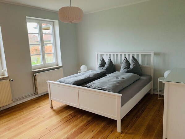 A bedroom with a white bed, grey bedding, a white headboard, a bedside table, and a hanging light fixture.