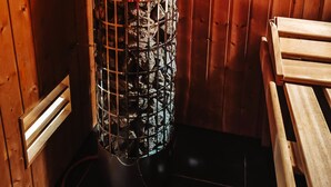 Eine Sauna mit einem Metallrost, der mit Steinen gefüllt ist, Holzwänden und einer Sitzbank.