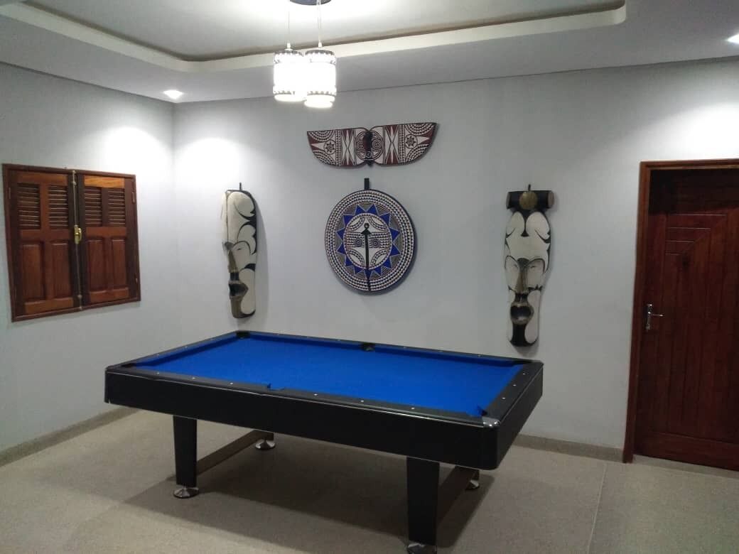 Una mesa de billar en una habitación con una puerta de madera, un adorno en la pared y una lámpara en el techo.