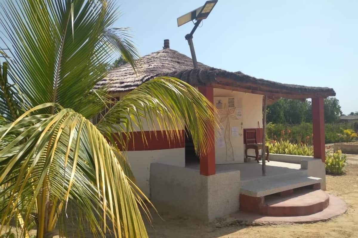Una pequeña construcción con techo de paja, un panel solar y un banco.