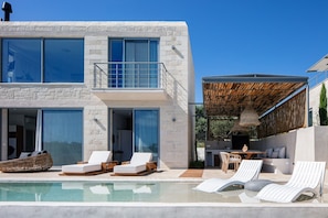 Moderni, kaksikerroksinen talo, jossa on uima-allas, ulkotila istumiseen ja katettu terassi.