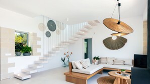 A modern living room with a staircase, a sofa, a coffee table, and decorative wall art. - BRAND NEW Lux Villa*Private Heated SaltyPool*BBQ*SeaView (Daratsos)