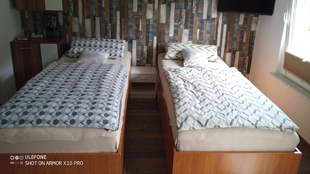 Une chambre avec deux lits, une armoire en bois, une étagère avec des objets décoratifs et un téléviseur fixé au mur.