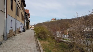 Une ruelle étroite pavée, bordée de bâtiments à l’architecture traditionnelle, un panneau de signalisation et, au loin, une vue sur une colline parsemée d’arbres.