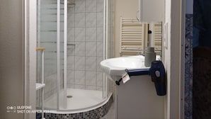 Une salle de bain avec une douche à parois de verre, un lavabo blanc doté d’un porte-serviettes et un sol carrelé.