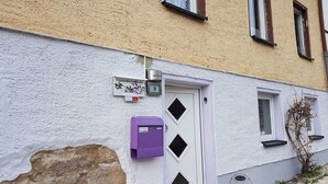 Un bâtiment à l’extérieur blanc, avec une boîte aux lettres violette et une porte portant un numéro.
