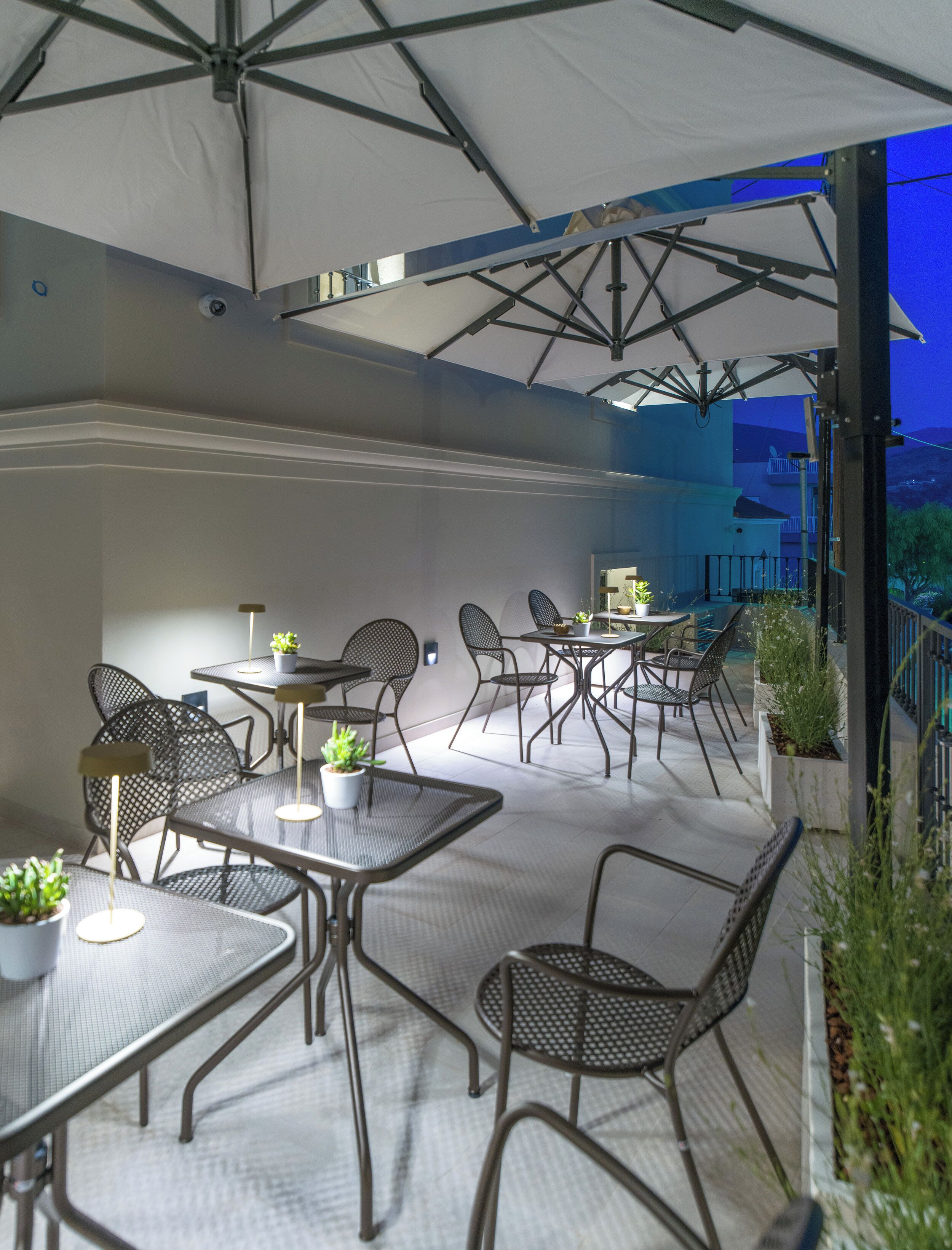 An outdoor patio area with multiple tables and chairs, umbrellas, and potted plants.