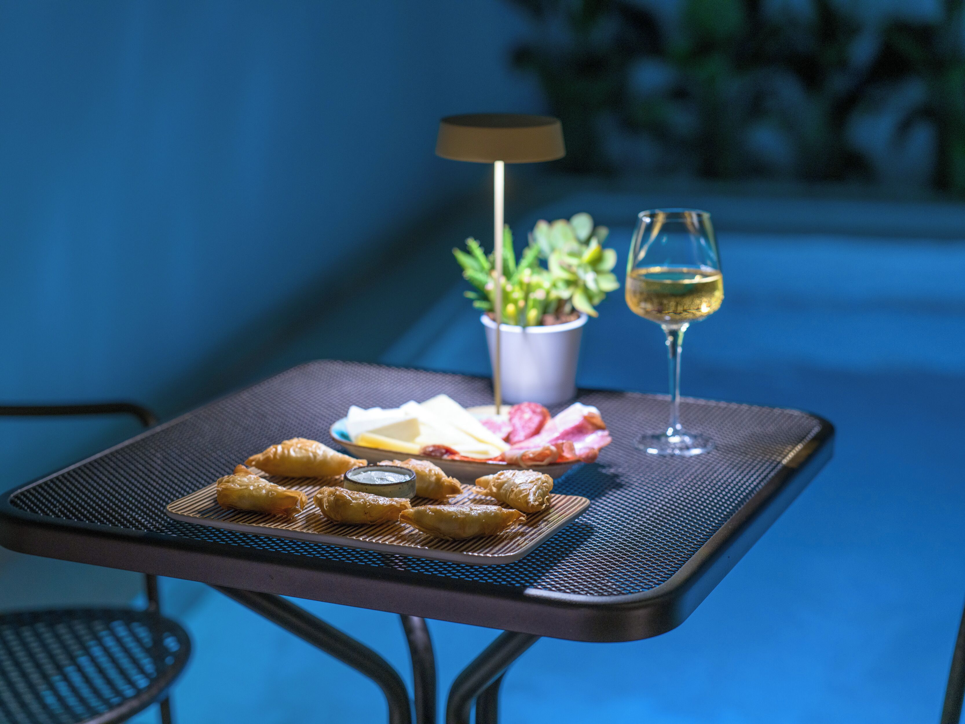 A table with a plate of pastries, a glass of white wine, and a small potted plant.