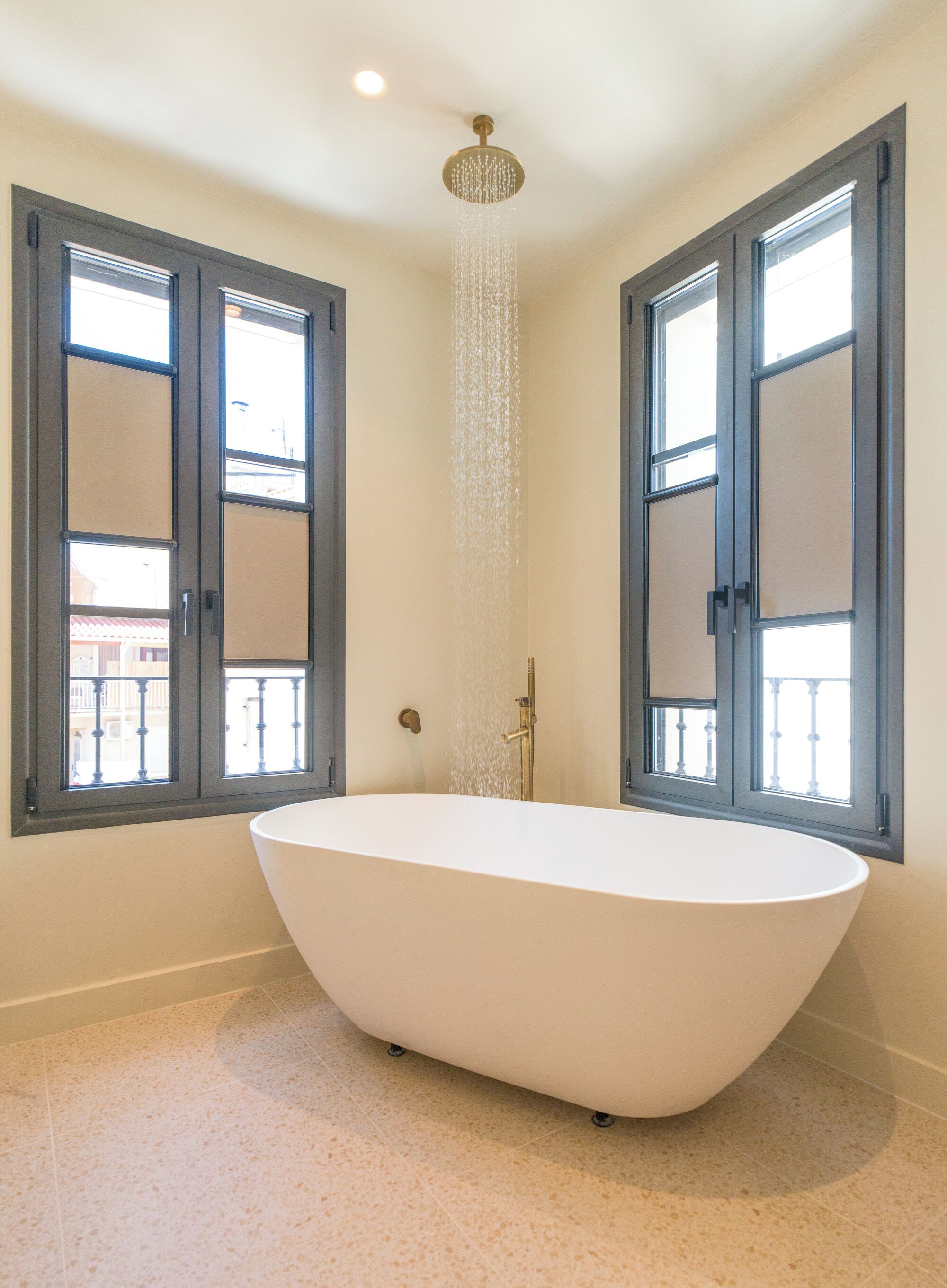 A modern bathroom with a freestanding bathtub, a showerhead, and large windows with dark frames.