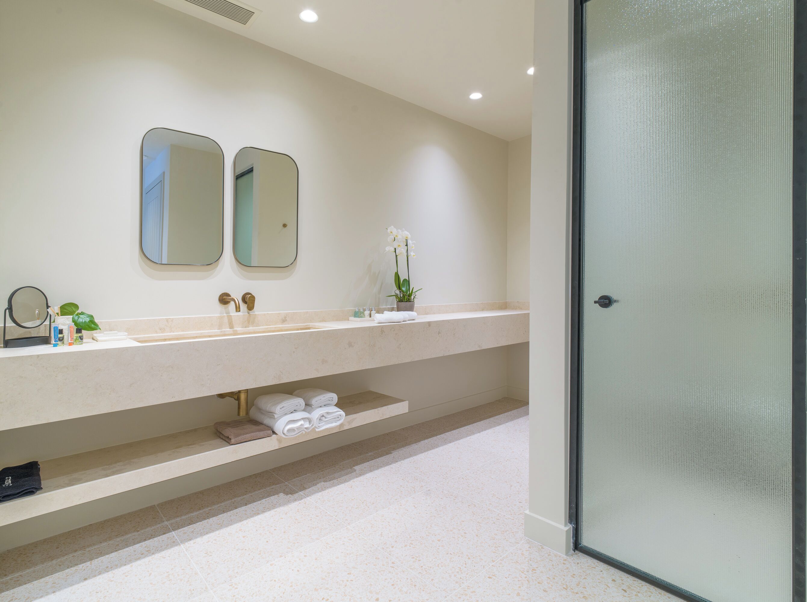 Un baño moderno con un lavamanos grande, dos espejos, una puerta de ducha de vidrio y un estante con toallas.