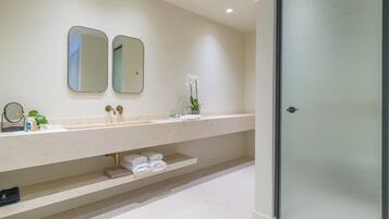 Un baño moderno con un lavamanos grande, dos espejos, una puerta de ducha de vidrio y un estante con toallas.