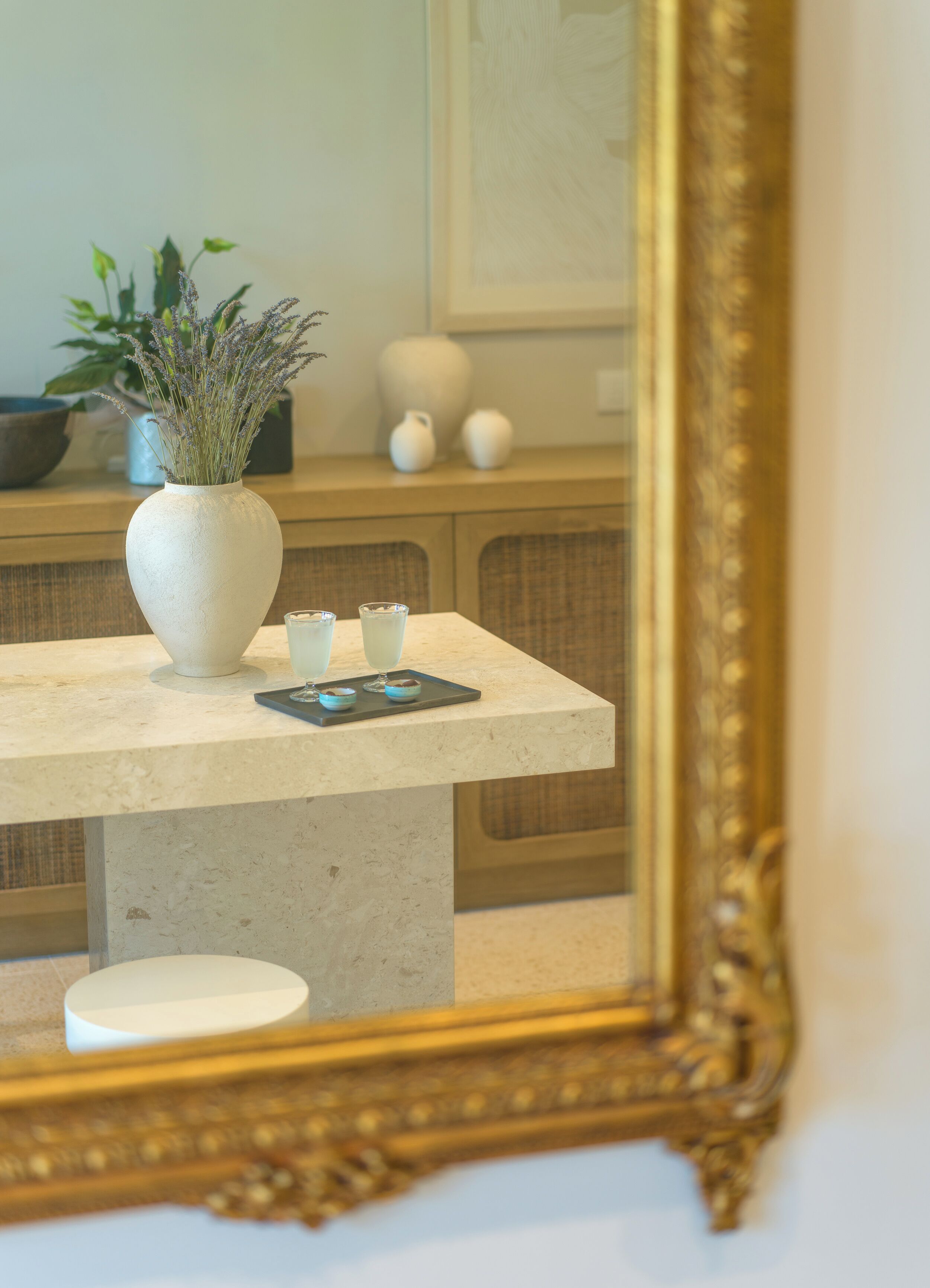 A room with a marble table, a white vase with lavender, and a gold-framed mirror.