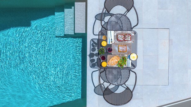 An outdoor dining area with a table and chairs by a swimming pool. - Argostoli Essence Suites (Kefalonia)