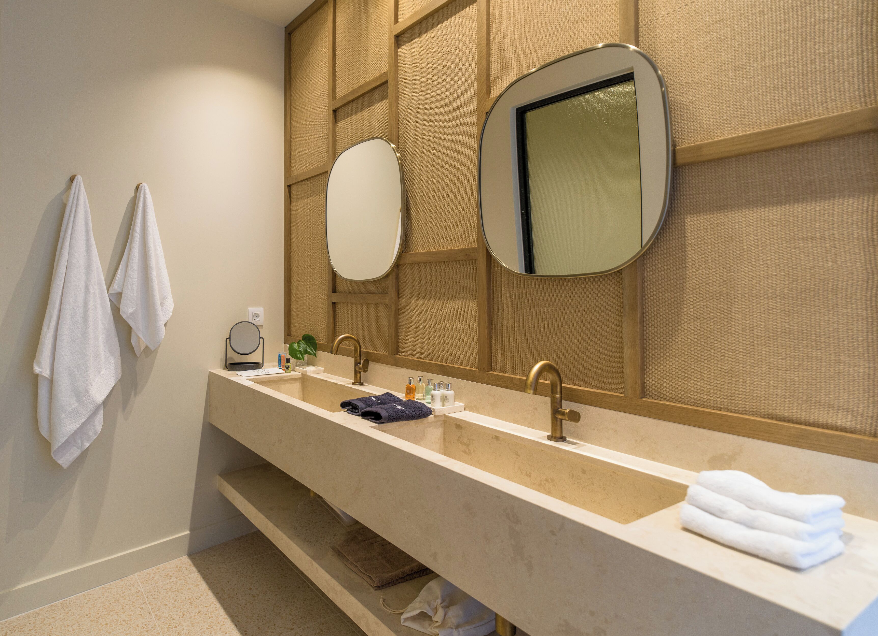 Un baño moderno con un lavamanos alargado, dos grifos, un espejo grande y un perchero para toallas.