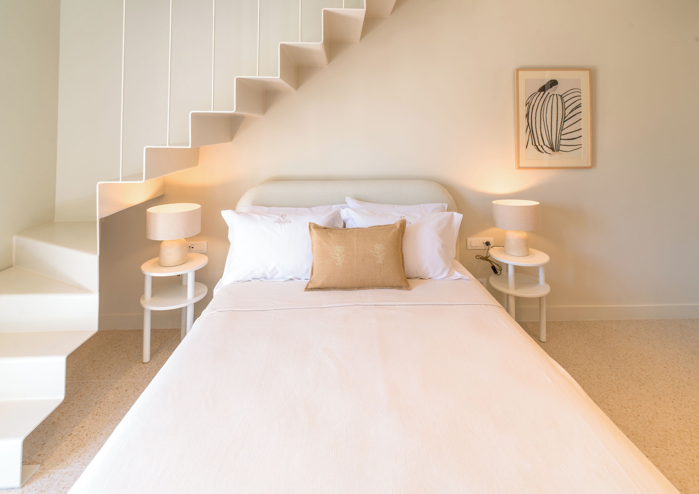 Une chambre à coucher comprenant un lit, deux tables de chevet, une commode, un escalier et une œuvre d’art encadrée accrochée au mur.