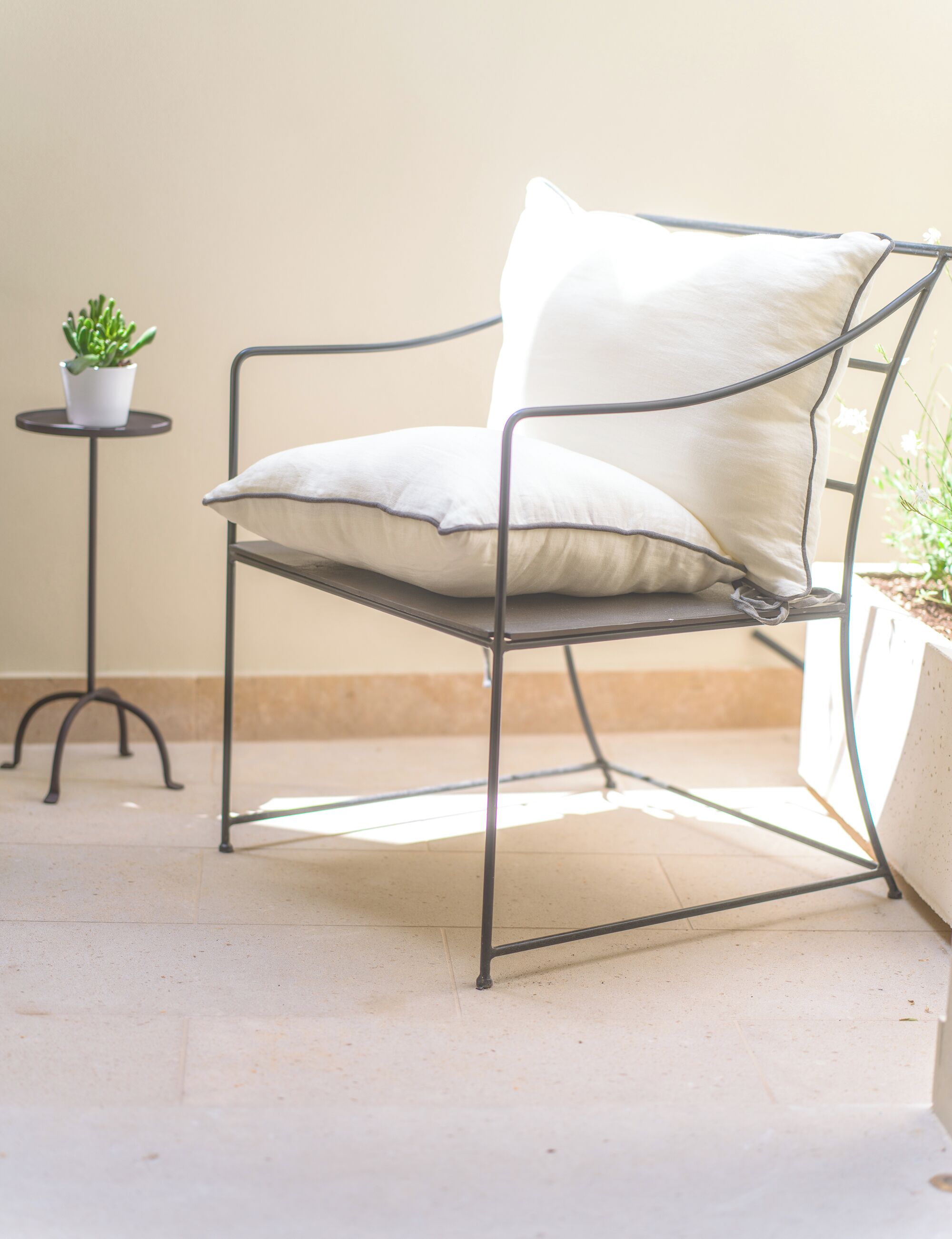 A metal-framed chair with cushions, a small round table with a potted plant, and a tiled floor.