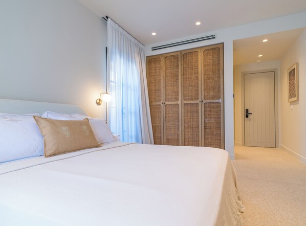 Een slaapkamer met een groot bed, een kast, een deur en een wandlamp.
