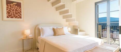 Ein Schlafzimmer mit einem großen Bett, einem Nachttisch, einem Sessel, einer Treppe und einem Balkon mit Blick.
