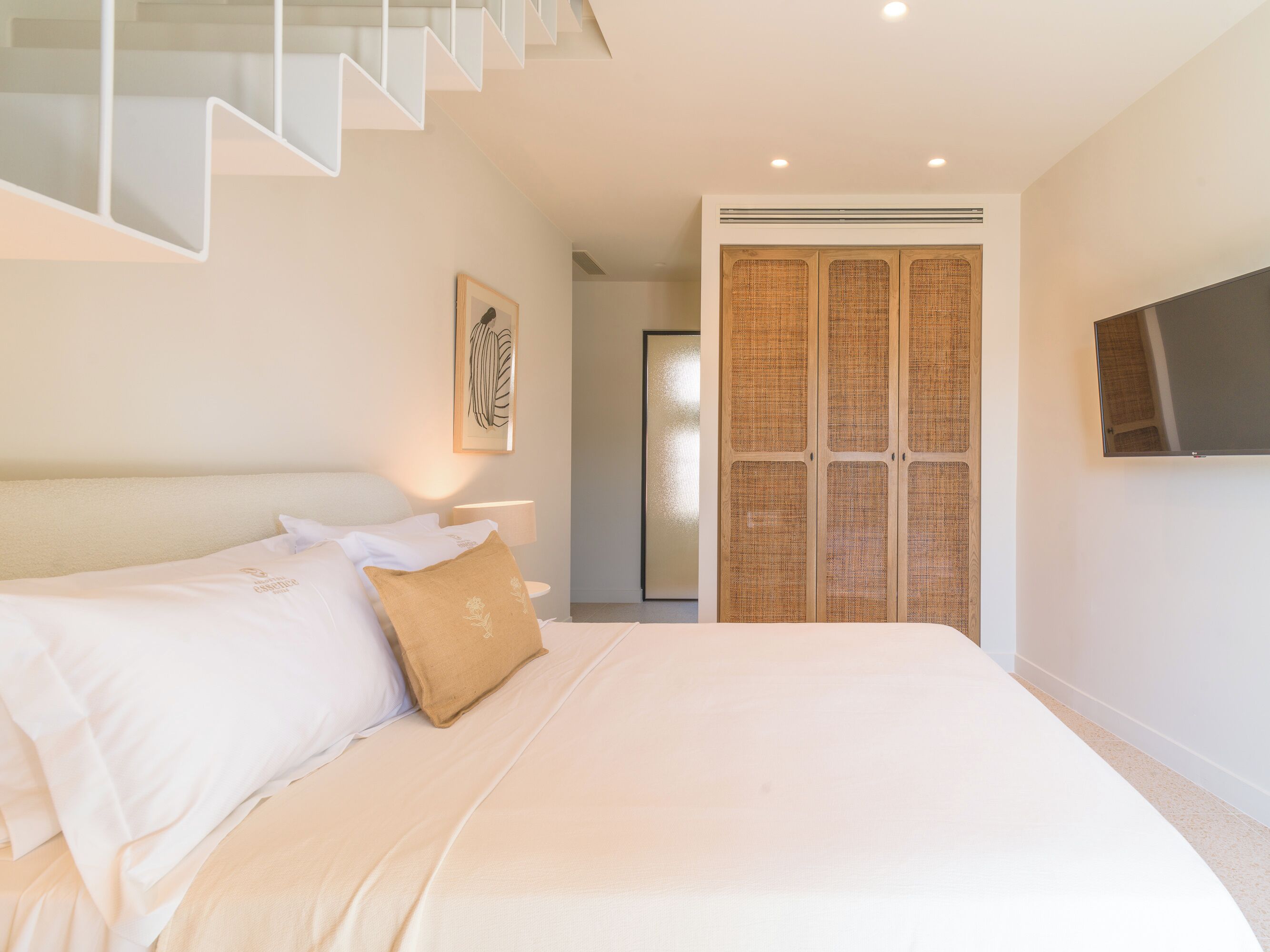 A modern bedroom with a large bed, a staircase, a wardrobe, and a television.