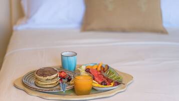 A breakfast tray with pancakes, fruit, and orange juice on a bed with white bedding and a brown pillow.