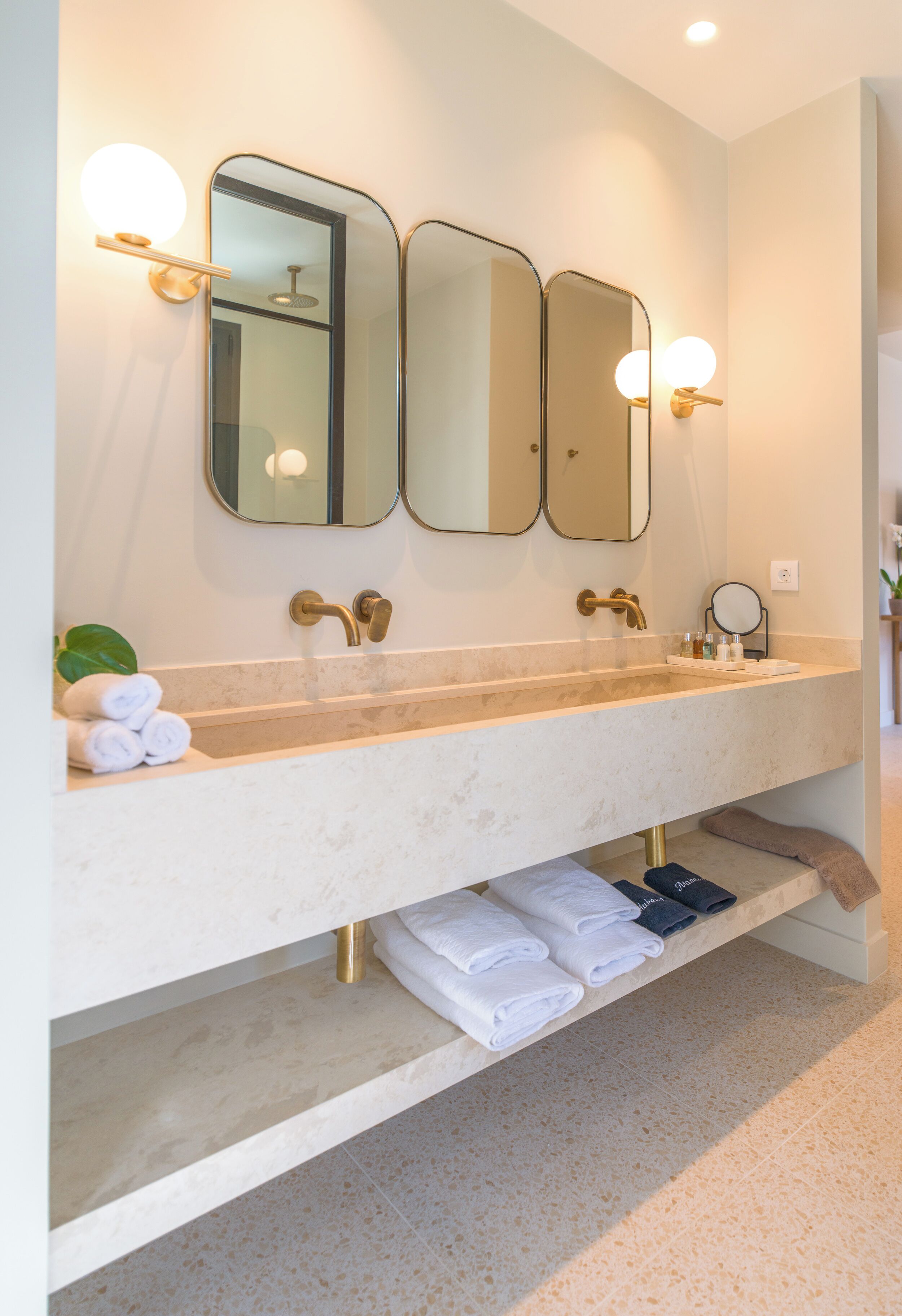 A bathroom with a large sink, three mirrors, and a towel rack.