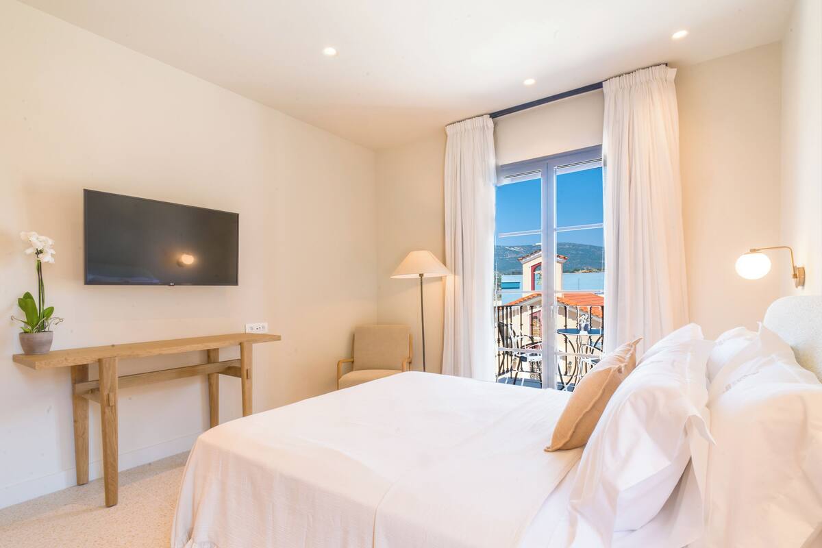 Une chambre d’hôtel avec un lit, un bureau, une chaise, une télévision et un balcon avec vue.