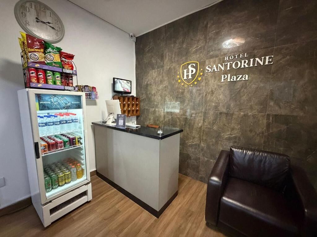 Uma mesa de recepção, um refrigerador com bebidas, um relógio e uma poltrona de couro em um saguão de hotel.