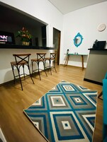Uma cozinha moderna com bancada preta, três cadeiras de madeira, um tapete azul e branco estampado e uma mesa pequena com espelho.