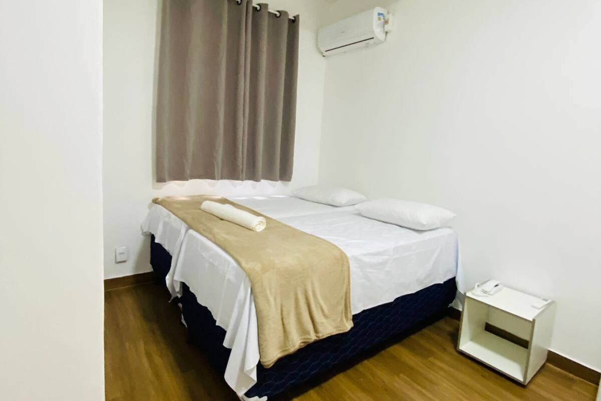 A neatly arranged bedroom with a bed, a bedside table, a wall-mounted air conditioner, and a curtain.