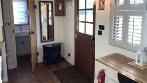 Un hall d’entrée accueillant avec une porte en bois, un miroir, une petite étagère en bois et un extincteur.