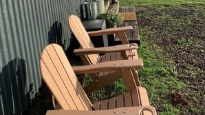 Il s’agit d’une petite construction en bois, recouverte de tôles ondulées, avec une porte en bois et une fenêtre. On y trouve à l’extérieur deux chaises en bois, un barbecue en métal et un pot de fleurs.