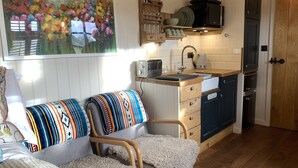 Une cuisine chaleureuse avec des meubles en bois, un four encastré et un évier. Un tableau coloré orne le mur, et un banc agrémenté de coussins à motifs est installé dans la pièce.