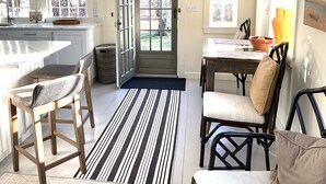 A kitchen with a large window, a dining area with chairs, and a black hanging light fixture. - Barn/cottage (Nantucket)