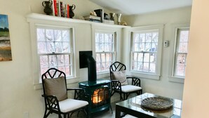 A cozy room with a fireplace, two chairs, a table, and large windows. - Barn/cottage (Nantucket)