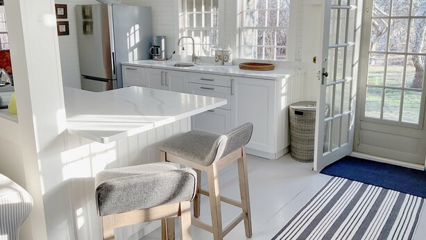 A bright kitchen with white cabinetry, a large island, and a view of the outdoors through a glass door. - Barn/cottage (Nantucket)