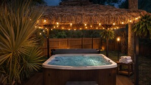 A hot tub with a wooden deck, surrounded by a wooden fence and tropical plants. - Heated Pool • Sauna • Hot Tub • Game Room • Beach • Golf Cart • Sleeps 15 (Port St. Joe)