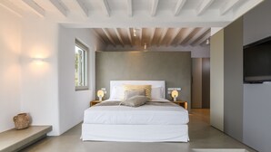 A modern bedroom with a large bed, bedside lamps, and a TV. - VILLA FAROS NEAR PORT, MYKONOS BY MYKONOS AGENDA (Mykonos)